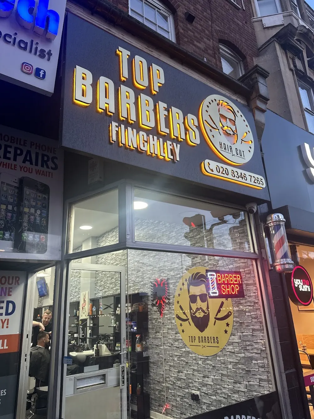 The lit yellow TOP BARBERS FINCHLEY sign at night